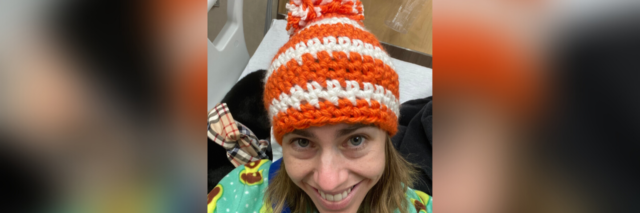 Photo of the author, wearing a homemade, orange and white striped crocheted hat from bed