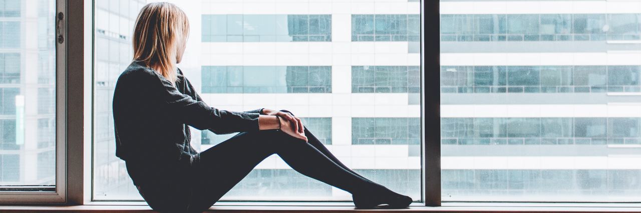What the Window of Tolerance Is and How Mental Illness Affects It woman with blonde hair sitting inside a building on a ledge looking out the window
