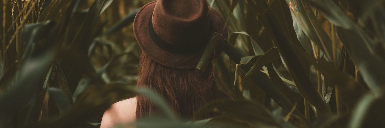back of a woman in brown hat in the middle of a field with leaves around her