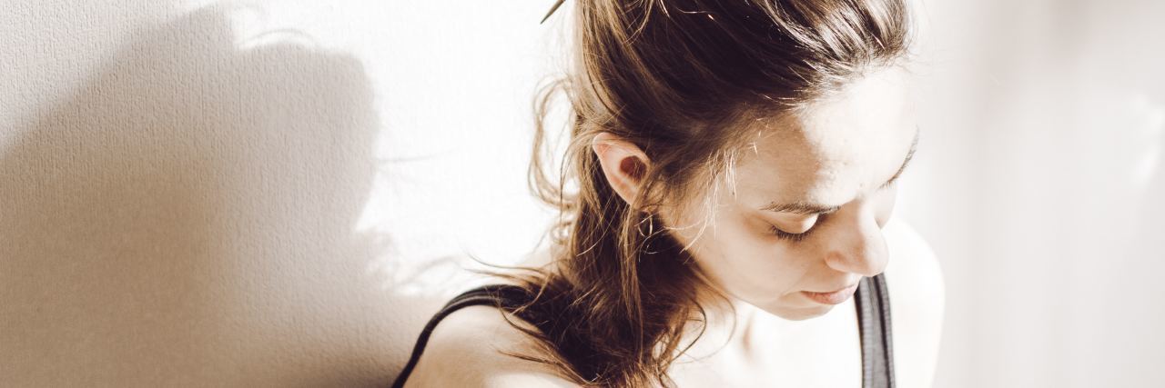 How to Avoid Affecting Loved Ones in Eating Disorder Recovery photo of woman against white wall bathed in sunlight, looking down