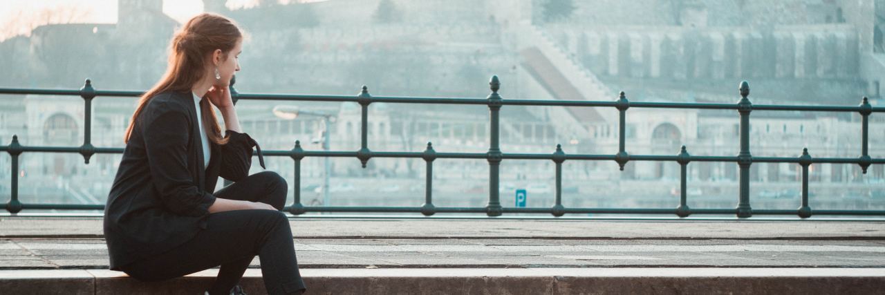 Depression Makes Me Shut People Out photo of woman sitting on steps looking at a city in background
