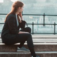 photo of woman sitting on steps looking at a city in background