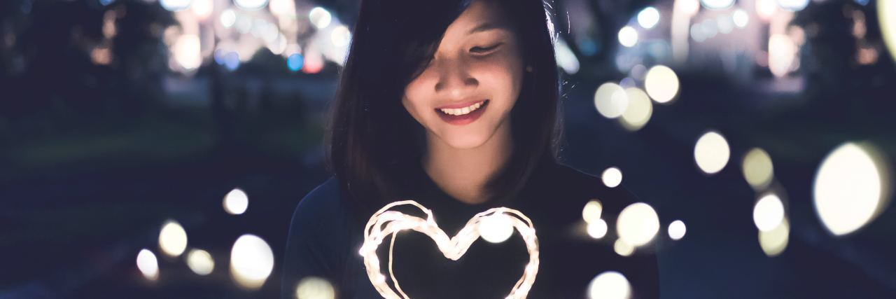 What to Know If Life Changes Are Affecting Your Mental Health photo of woman looking down at a heart made out of light in her hands, smiling and surrounded by other lights