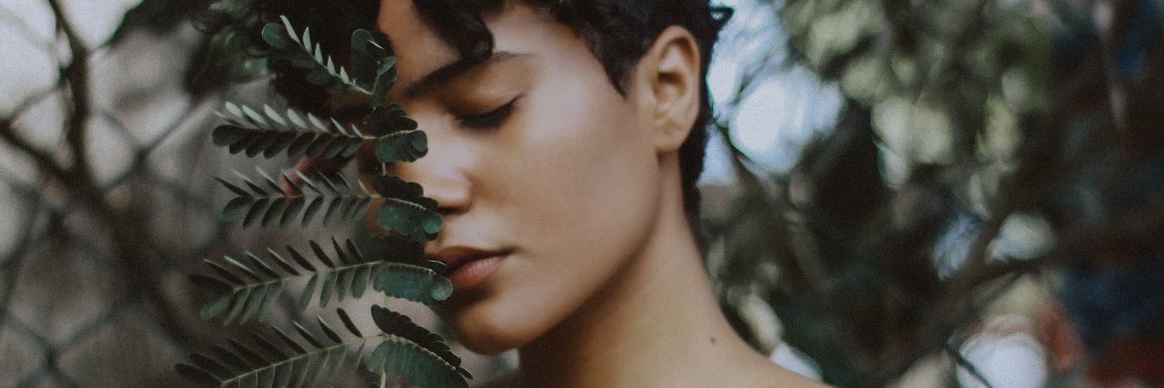 What Happened When I Realized I No Longer Need Trauma Therapy photo of woman with short hair standing next to large leaves with eyes closed