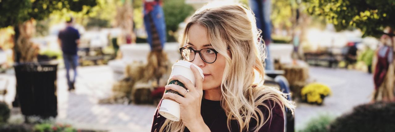 Woman drinking coffee in an outdoor courtyard.