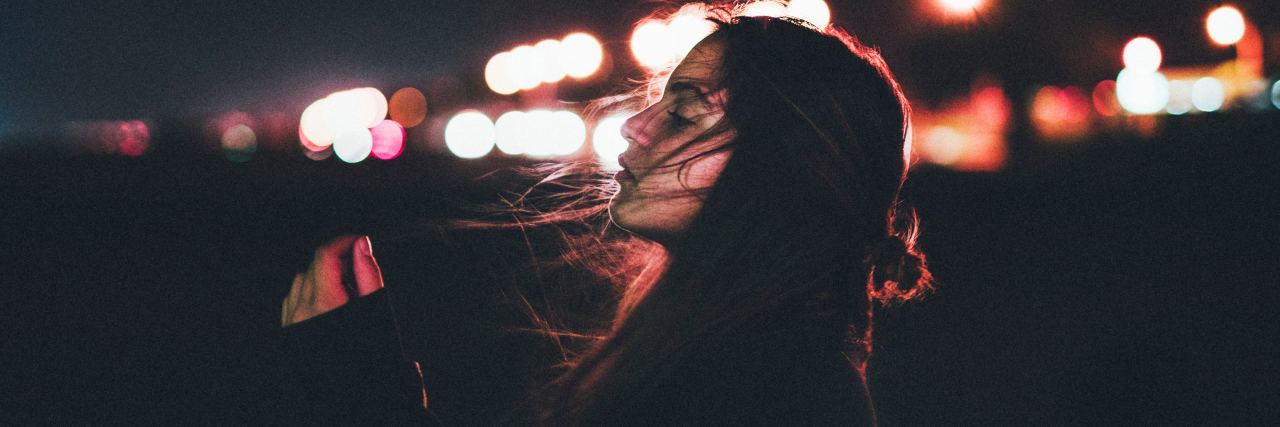 This Is What Happens When People Can’t ‘See’ Your Chronic Illness A woman standing in front of blurred city lights at night