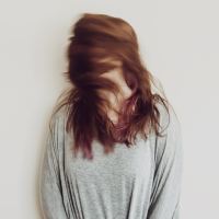 photo of woman standing against plain white wall, turning head fast so that her head is blurred and her hair covers her face