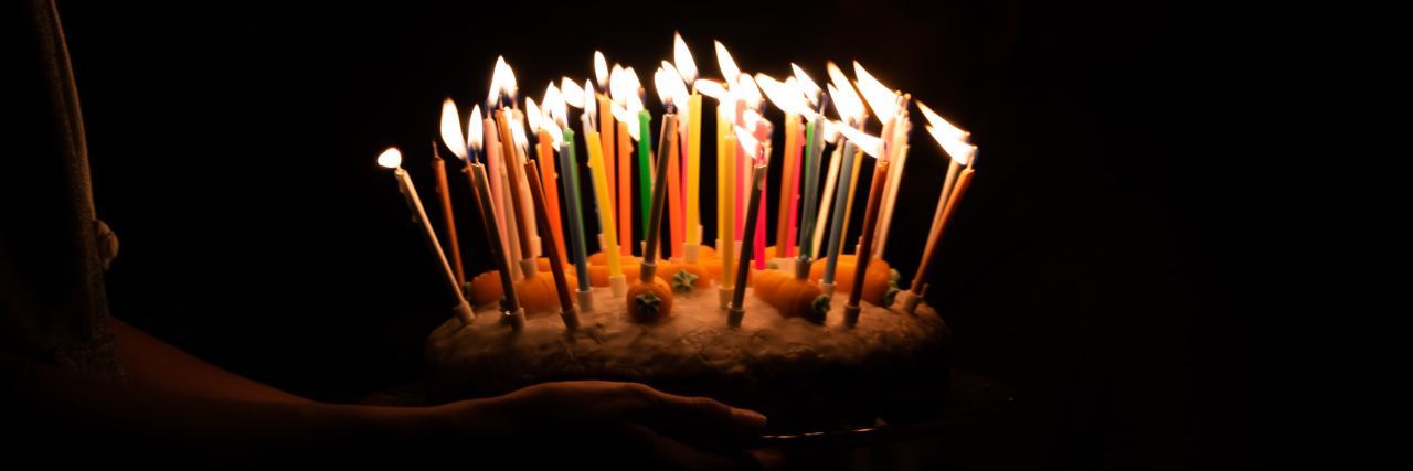 person carrying a birthday cake with many candles lit in the dark