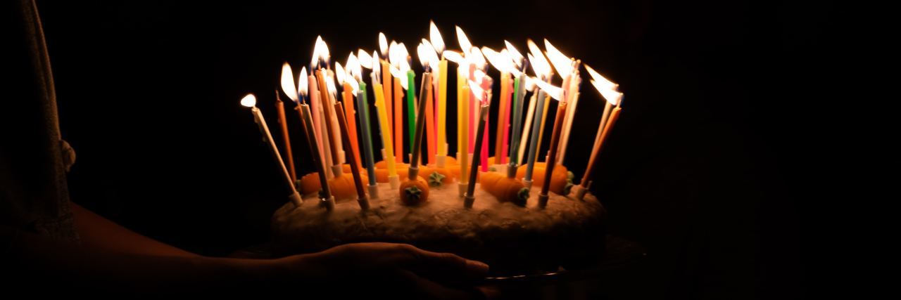 I Celebrate My Birthday as a Suicide Attempt Survivor for My Mom person carrying a birthday cake with many candles lit in the dark