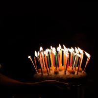 person carrying a birthday cake with many candles lit in the dark