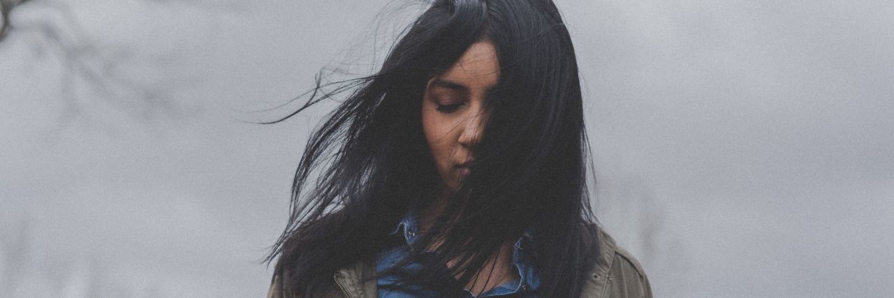 woman outside with black hair blowing over her face looking down