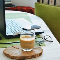 Computer on a desk with a pair of classes and cup of coffee on a wooden coaster nearby