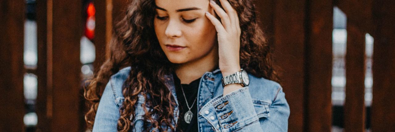 photo of woman with hand raised to her hair, looking down, sad or upset