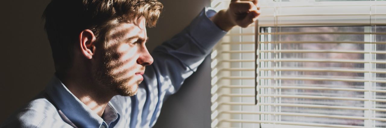 photo of man looking out of window with unhappy expression
