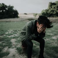 photo of man kneeling over and covering face in the middle of a field