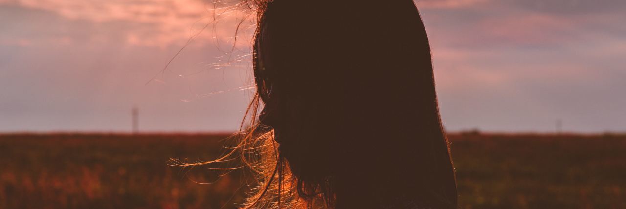 Why I Went on Disability for Bipolar and What to Know About Applying woman standing sideways to camera, hair in her face in a field with the sunset in the background