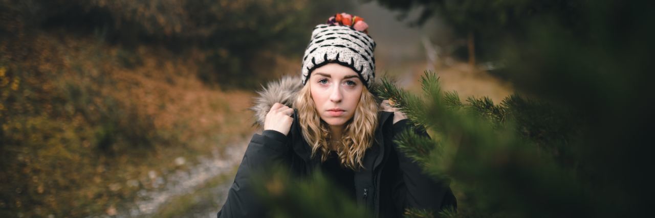 How I Find Hope With PTSD Even Though I'm Scared of My Resiliency woman with winter hat on in the road staring at camera behind a tree