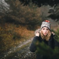 woman with winter hat on in the road staring at camera behind a tree