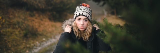 woman with winter hat on in the road staring at camera behind a tree