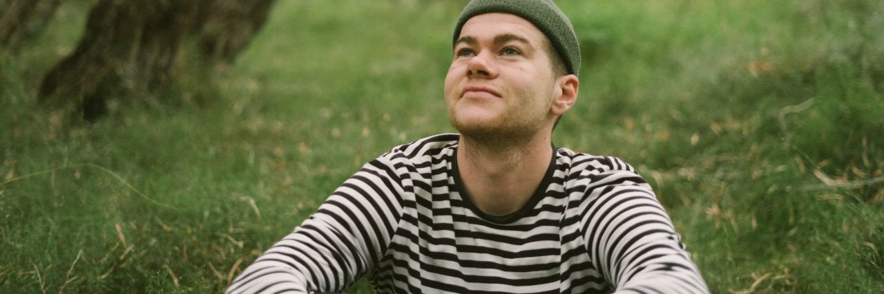Should I Still Go to Therapy If I Have Nothing to Say Today? photo of man in black and white striped t-shirt sitting on long grass by a tree, looking peaceful
