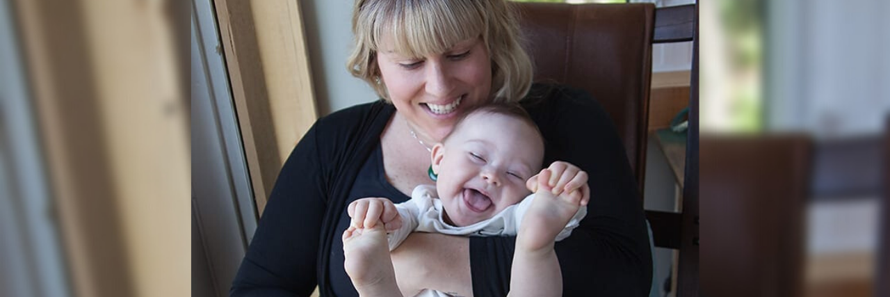 Responding to Doctors With a Negative View of Down Syndrome Sarah holding her son Harvey, who has Down syndrome. He is laughing and holding his feet in his hands.
