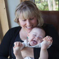 Sarah holding her son Harvey, who has Down syndrome. He is laughing and holding his feet in his hands.