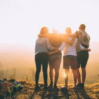 Group of friends with arms around each other, standing together at sunset