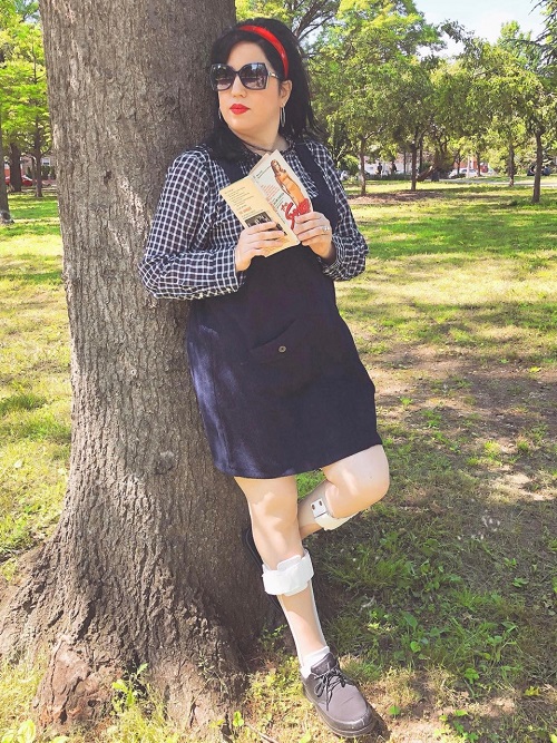 Daffny leaning against a tree. She is wearing a skirt, and her leg braces are visible.