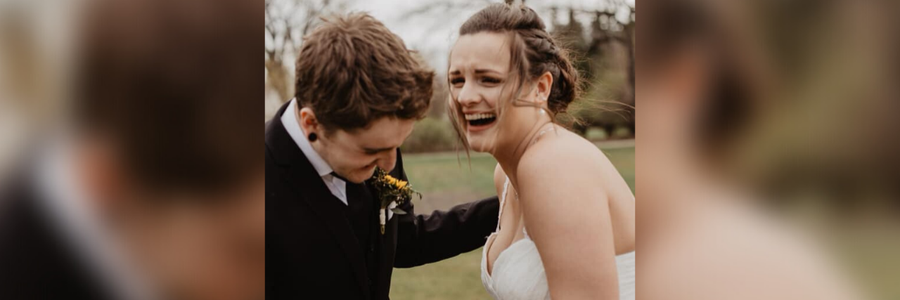 A man in a suit and a woman in a wedding dress laughing together outside