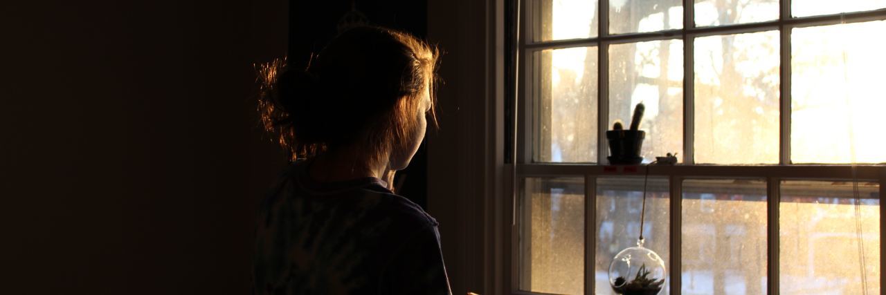 woman in a dark room looking outside her window with snow and light