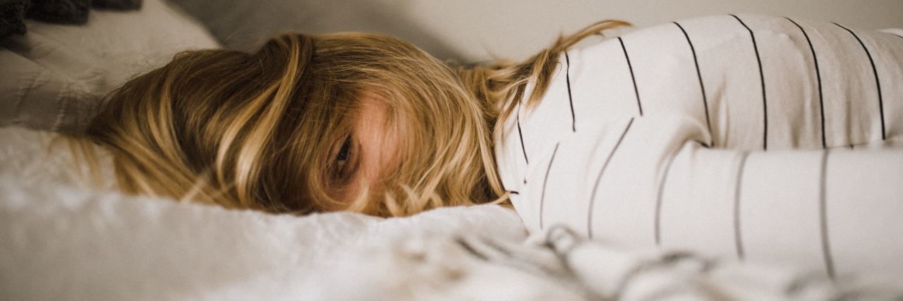 What Anxiety Is Like in the Morning and Tips to Make Mornings Easier woman lying in bed, hair in her face, turned to the camera