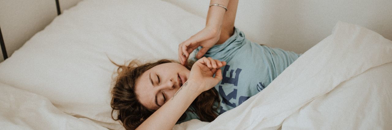 25 Things People With Chronic Illness Will Understand young woman in bed waking up, arms stretching out
