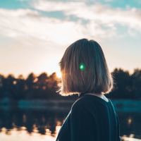 woman with short hair looking out at a lake at sunset