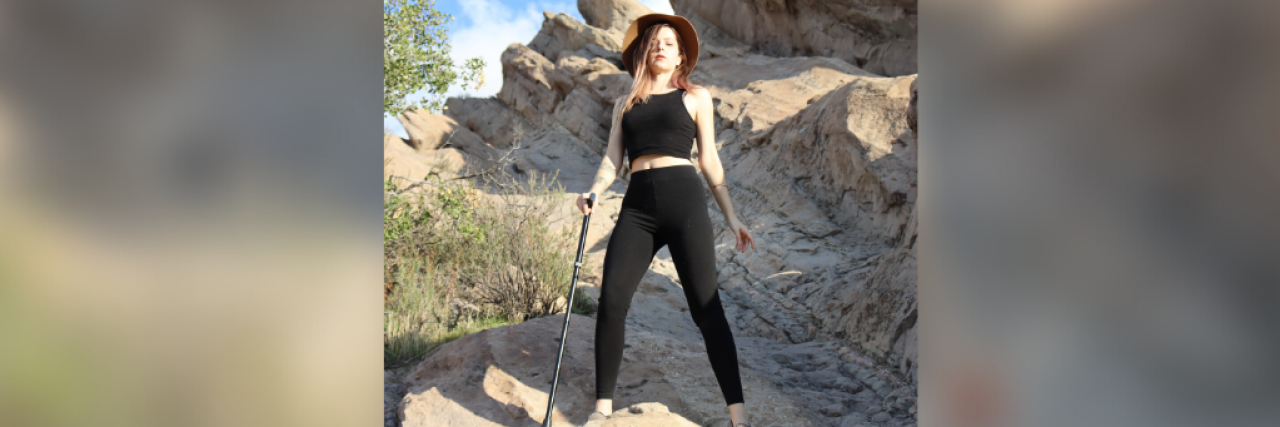 Embracing the Solitude of Living with Chronic Illness Woman standing proudly on a rock formation outside, holding a cane