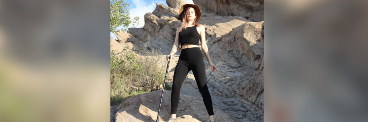 Woman standing proudly on a rock formation outside, holding a cane