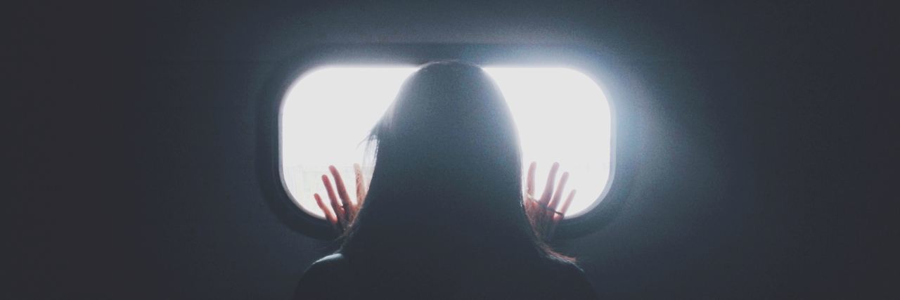 photo of woman taken from behind silhouetted looking out of tiny window