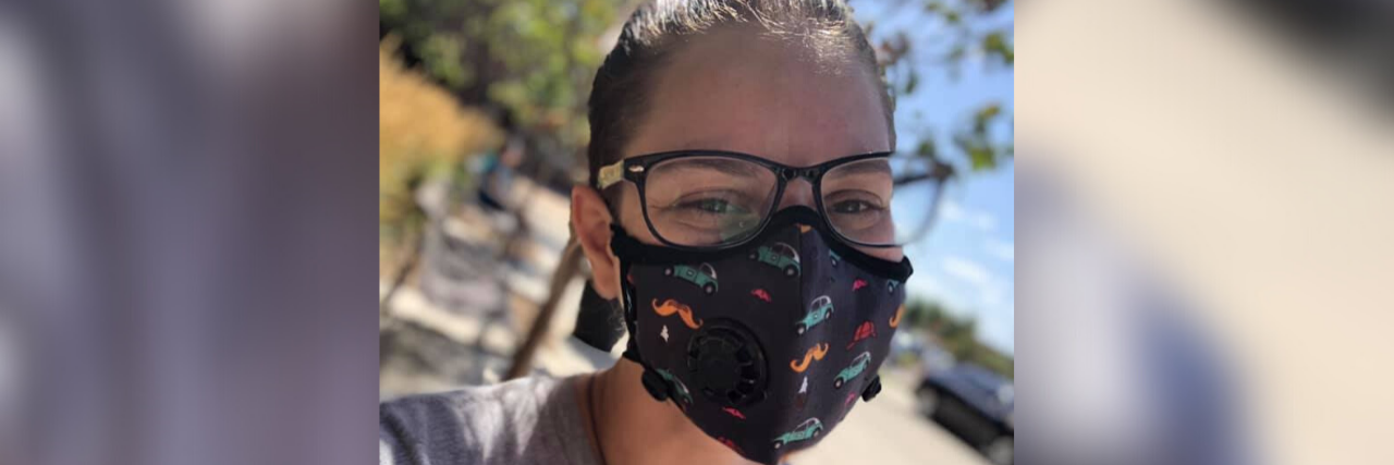 Being Accused of Faking My Disability as an Ambulatory Wheelchair User Marisa wearing a Vog mask with a cheerful car pattern on it.