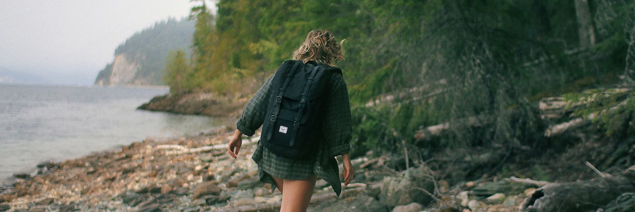 How Travel Has Influenced My Eating Disorder Recovery Woman wearing a backpack and walking on a rocky beach