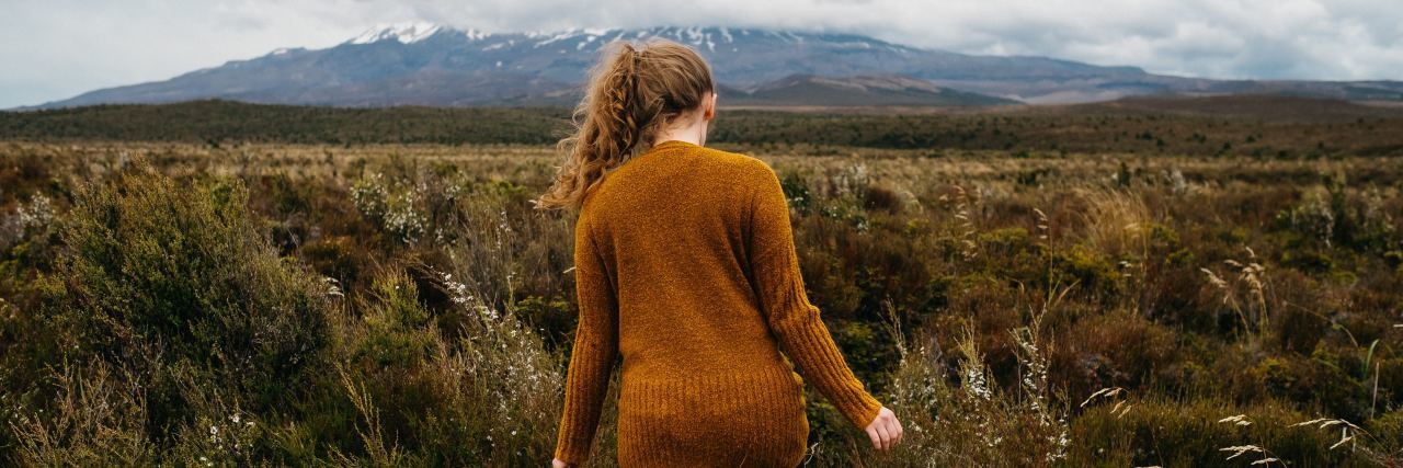 How to Stick to Healthy New Year’s Resolutions photo of woman walking through field toward mountain in the distance