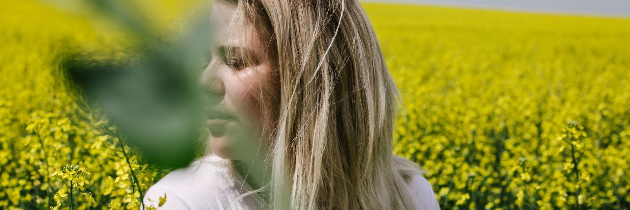 photo of blonde woman sitting in field of yellow flowers, looking away from camera, with a large leaf covering her face