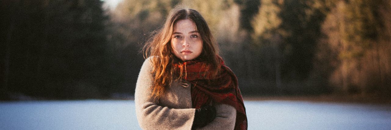 In My Darkest Depression, I Fought for Myself Through Therapy woman standing outside in the winter on snowy ground in a jacket with arms folded looking at camera