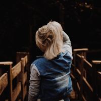 woman on a wooden bridge in the dark with her back facing the camera, holding her blonde hair up in her hand