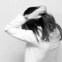 black and white photo of woman facing away from camera, covering head with her hands