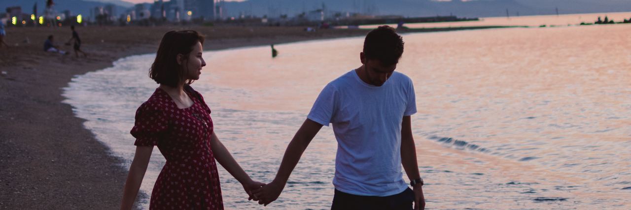 What to Know About Loving Someone With PTSD photo of couple on a beach at sunset standing hand-in-hand, man walking into water