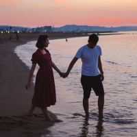 photo of couple on a beach at sunset standing hand-in-hand, man walking into water