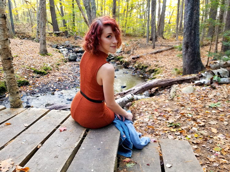 the author sitting in the woods near a creek, looking at the camera