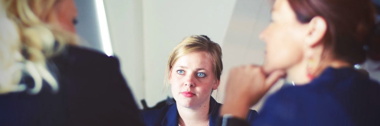 workplace, employee woman sitting across from 2 bosses who are consulting with each other