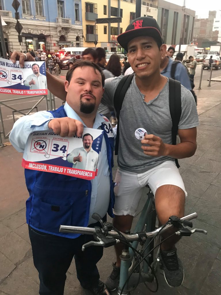 Bryan Russell stands next to a man on a bike holding a campaign sign and button