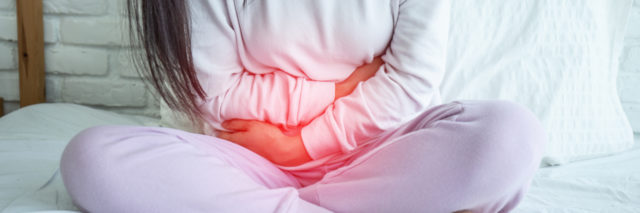 Woman sitting in bed holding her abdomen.