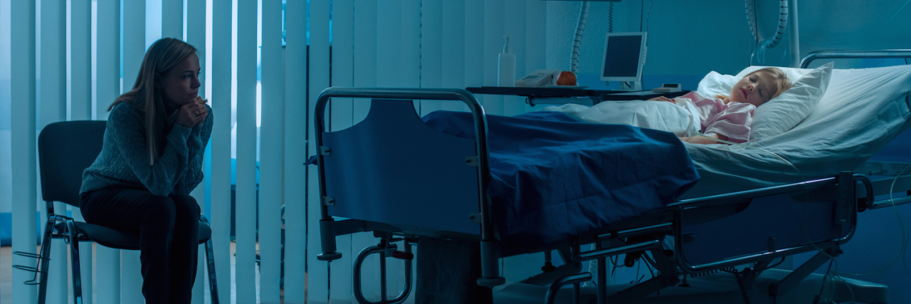 When Your Child Has a Complex Health Condition Young girl sleeping in hospital bed with her mother sitting in a chair next to her